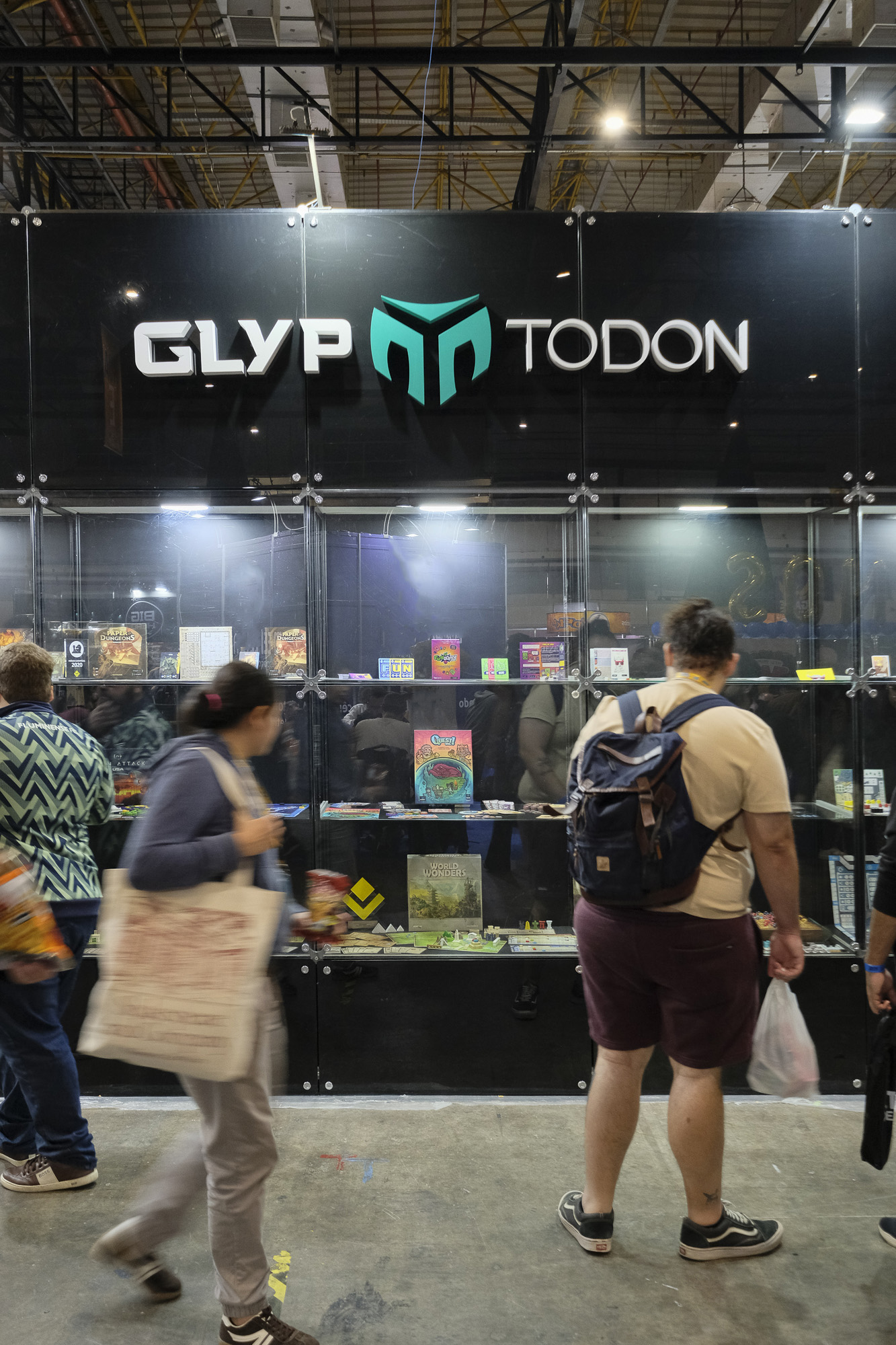 Vitrine Glyptodon Studio no DOFF 2025, com os jogos da coleção e alguns visitantes da feira observando.