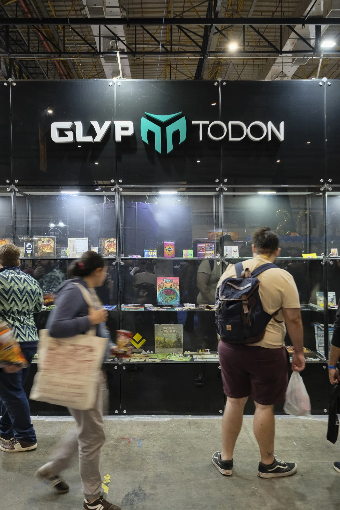 Vitrine Glyptodon Studio no DOFF 2025, com os jogos da coleção e alguns visitantes da feira observando.